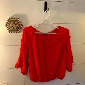 Orange blouse with macrame details on sleeve.